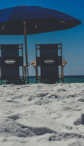 Two beach chairs under a blue umbrella on white Destin sand
