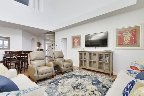 Open-plan living room with beige recliners, wall-mounted TV, wooden media cabinet, and patterned area rug