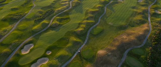 Aerial view of golf course fairways and bunkers at golden hour, cart path winding through the course