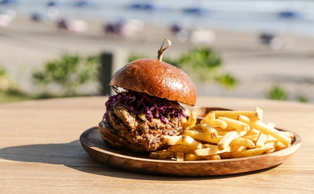 Burger and fries on a wooden plate at a casual beachside grill