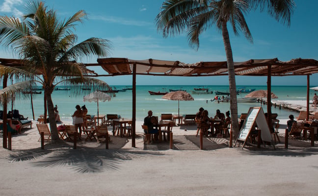 Beachfront restaurant with thatched roof, palm trees, and turquoise water