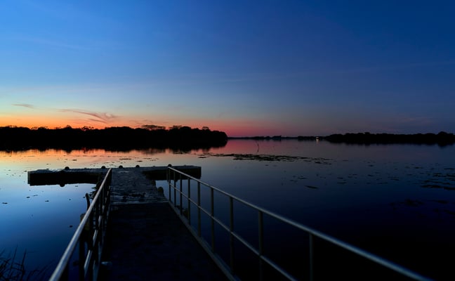Dock extending into calm water at dusk with a deep blue sky