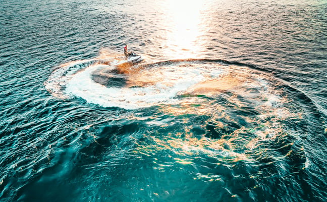 Aerial view of a jet ski spinning in turquoise water at sunset