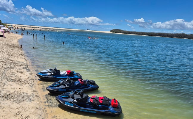 Jet skis lined up on a sandy beach with calm turquoise water